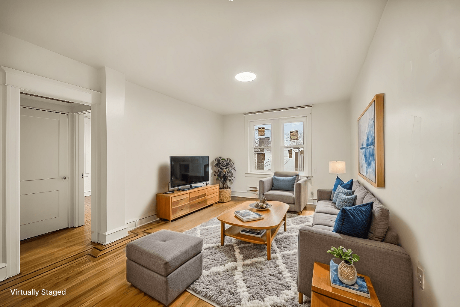 A living room with a grey couch, a brown ottoman, a wooden coffee table, and a television.